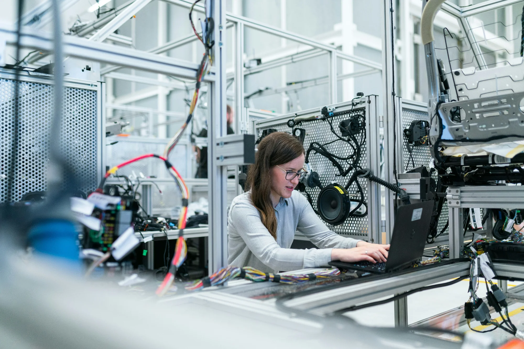 Female engineer working on laptop surrounded by wiring and hardware in a testing lab